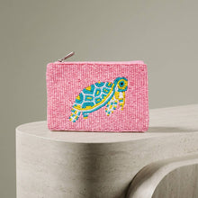 Load image into Gallery viewer, A pink beaded coin purse with a blue, white and yellow turtle on it. Placed on a grey stone platform with a grey background