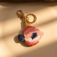 Load image into Gallery viewer, A gold, pink and blue beaded fish keychain with a beige background
