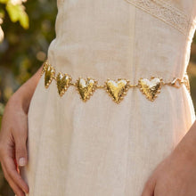 Load image into Gallery viewer, A gold-tone chain belt featuring textur4ed heart-shaped links, worn around the waist over a beige outfit, with a blurred outdoor background.