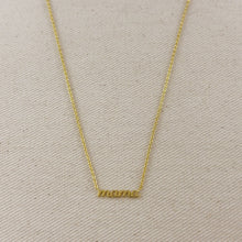 Load image into Gallery viewer, A delicate gold chain necklace with a small horizontal bar pendant engraved with the word 'MAMA', displayed on a textured beige fabric background.