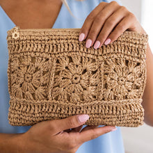 Load image into Gallery viewer, A close-up of a person holding a woven straw clutch bag with intricate floral crochet patterns and a gold zipper pull.