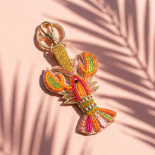 Load image into Gallery viewer, Orange, pink and multicolored crawfish beaded keychain with a pink background and shadows of leaves