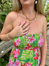 Load image into Gallery viewer, A woman wearing a colorful tropical floral strapless dress with green leaves and pink flowers, accessorized with gold necklaces and rings, standing outdoors on a wooden boardwalk.