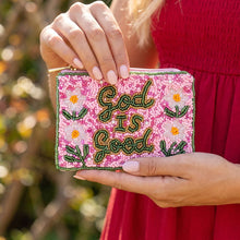 Load image into Gallery viewer, A pink and floral beaded coin purse with God is Good in green beads. A woman in a red dress is holding it outside with a blurred background