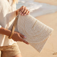 Load image into Gallery viewer, A woman on the beach wearing a white top and tan shorts holding an ivory clutch