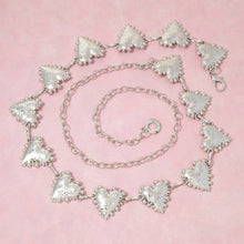 Load image into Gallery viewer, A silver-tone chain belt featuring multiple textured heart-shaped links with beaded edges and an adjustable chain extension, displayed on a light pink background.