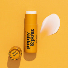 Load image into Gallery viewer, A yellow Poppy & Pout lip balm stick labeled 'Wild Honey' is shown on a warm yellow background with the cap beside it and a white cream smear to the right.