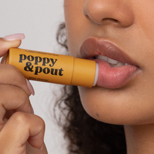Load image into Gallery viewer, Person applying a Wild Honey lip balm labeled 'Poppy & Pout' to their lips.
