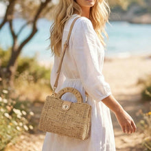 Load image into Gallery viewer, A woman in a white dress carrying a woven straw handbag with a shoulder strap, photographed outdoors near the beach.

