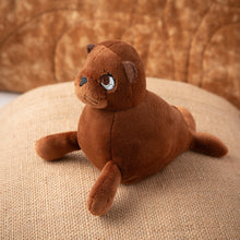 Load image into Gallery viewer, A small sea lion squishy plush sitting on a tan pillow with a brown background.
