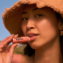 Load image into Gallery viewer, Woman applying Poppy &amp; Pout pink grapefruit lip balm with a straw hat on a sunny day
