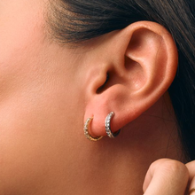 Load image into Gallery viewer, Close-up of an ear wearing two cz hoop earrings one gold and one silver with a blurred background
