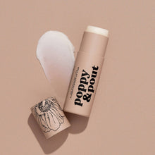 Load image into Gallery viewer, A beige Island Coconut cosmetic stick product labeled 'poppy &amp; pout' with its cap placed beside it on a matching beige background, with a white product smear behind it.
