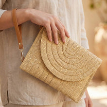 Load image into Gallery viewer, A woman holding a tan and golden clutch with a beige shirt on and a blurred background
