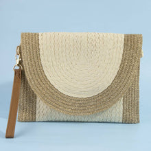Load image into Gallery viewer, A woven straw clutch bag with a semi-circular flap in cream and natural beige, featuring a brown leather wristlet strap and gold-tone hardware, set against a solid light blue background.
