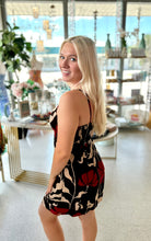 Load image into Gallery viewer, A blonde woman wearing a sleeveless black dress with a red and beige floral pattern, posing in a brightly lit boutique interior.
