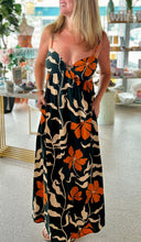 Load image into Gallery viewer, A close up of a woman wearing a dark green maxi dress with cream and orange leaf and floral patterns, with two rings connecting both sides in the front breast.
