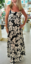 Load image into Gallery viewer, A close up of a woman wearing a black and white hibiscus maxi dress, with the background being a bright boutique.
