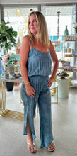 Load image into Gallery viewer, A woman modeling a light navy blue jumpsuit featuring thin straps, a v-neckline, and a flow silhouette, standing in a bright boutique.
