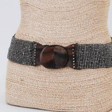 Load image into Gallery viewer, A grey metallic beaded belt with a wooden buckle on a woven tan mannequin with a light grey background
