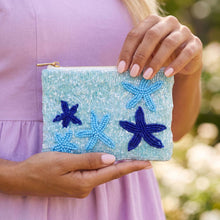 Load image into Gallery viewer, A light blue and dark blue beaded coin purse with 5 starfish on it.  A woman with pink nails and a purple dress is holding it with a blurred background.  

