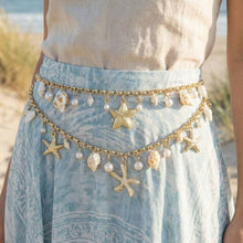 Load image into Gallery viewer, Gold chain belt with starfish and shell charms on a light blue skirt by a beach.
