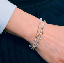 Load image into Gallery viewer, Close-up of a wrist wearing multiple blue and pearl beaded bracelets on a dark background
