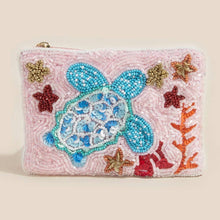 Load image into Gallery viewer, A pink beaded zip pouch featuring a large blue and white beaded sea turtle design, surrounded by colorful beaded starfish and coral motifs on a light beige background.
